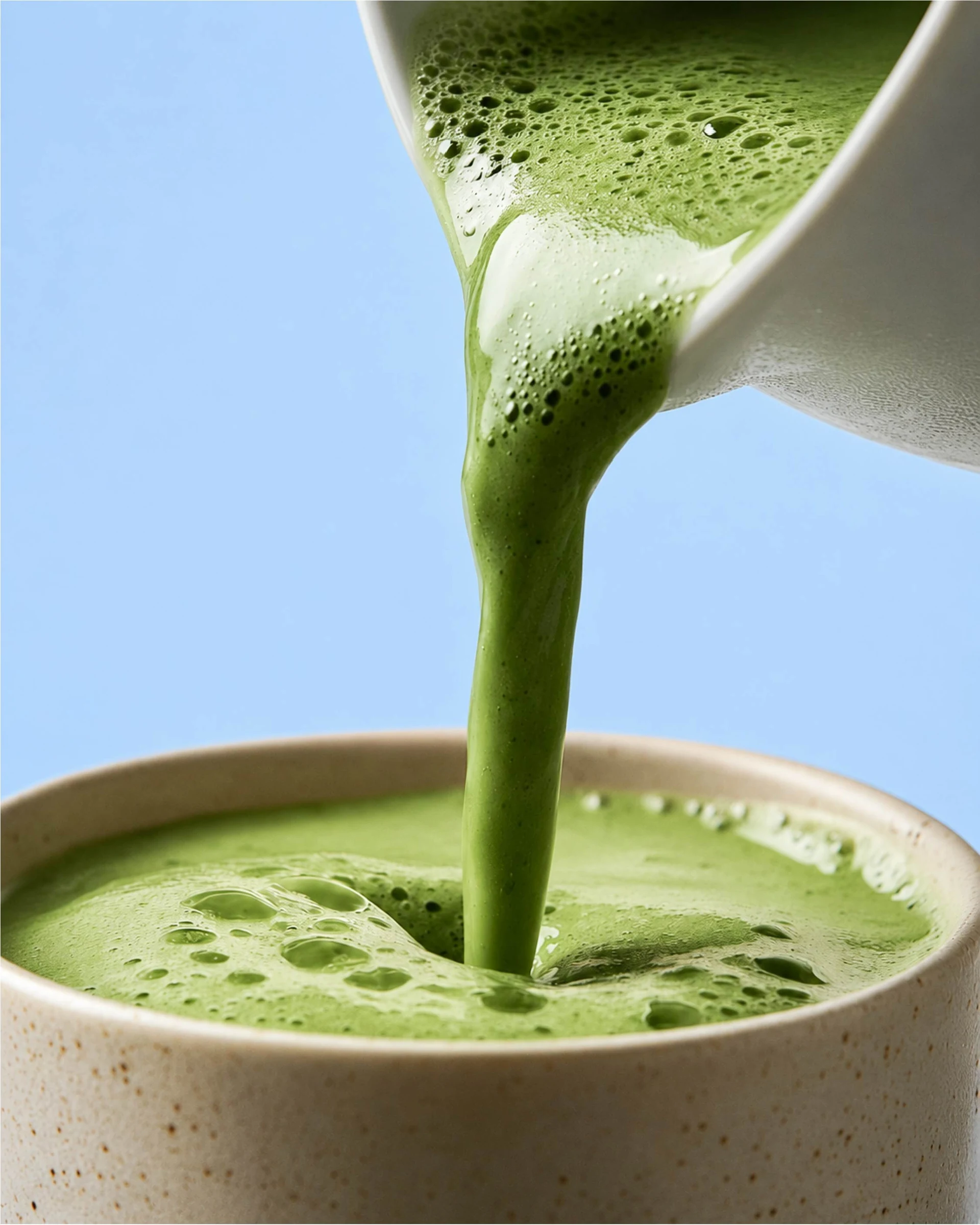 Grön matcha hälls från en vit kanna ner i en skål.