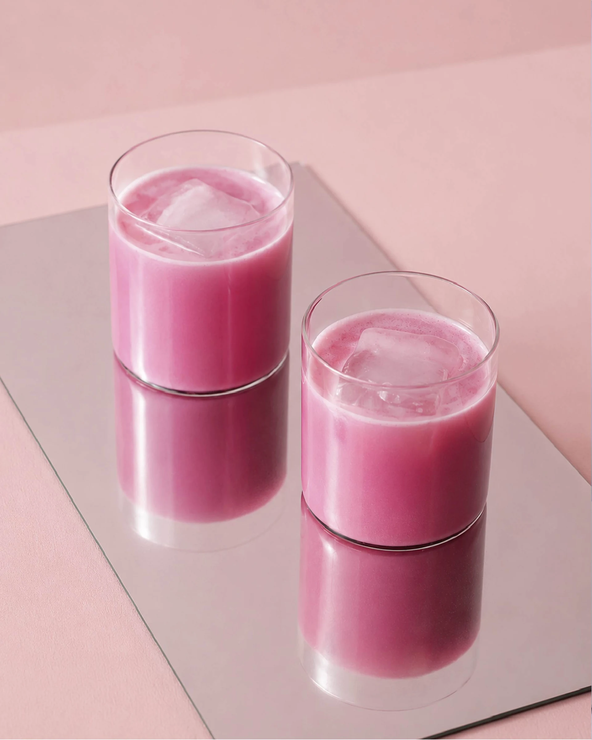 Två glas med rosa lattedryck och is mot en rosa bakgrund.
